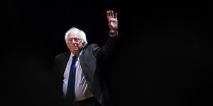 Bernie Sanders vor schwarzem Hintergrund, hebt die Hand