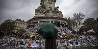 Eine Person steht mit einem Regenschirm auf dem Place de la Republique und schaut an das Denkmal für die Toten der Terroranschläge vom 13. November
