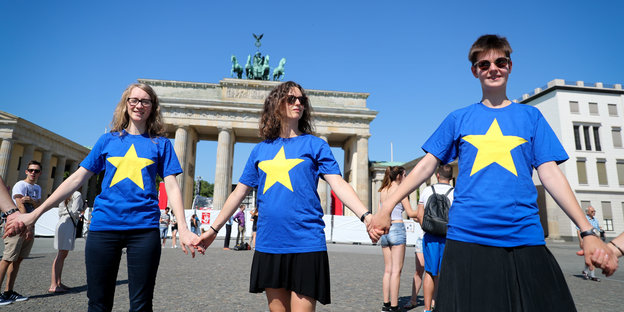 Menschen tragen blaue Tshirts mit gelben Sternen und reichen sich vor dem Brandenburger Tor die Hände