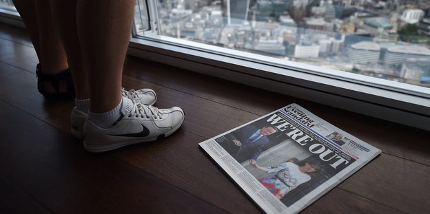 Füße neben einer Zeitung vor einem Fenster.