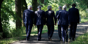 Sechs Männer gehen auf einem Waldweg, man sieht sie von hinten