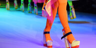 Hochhackige Schuhe in Orange mit ebensolchen Strümpfen gehen über einen Laufsteg