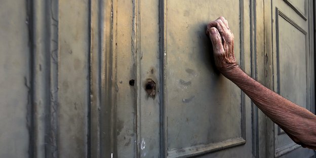 Der Arm eines alten Menschen an eine graue Tür gelehnt