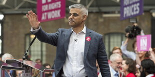 Ein Mann in Hemd und Jackett hebt die Hand zum Gruß, es ist Sadiq Khan