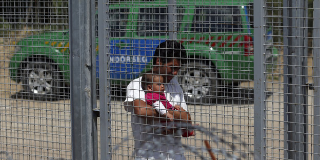 Ein Mann mit Baby im Arm hinter einem Zaun