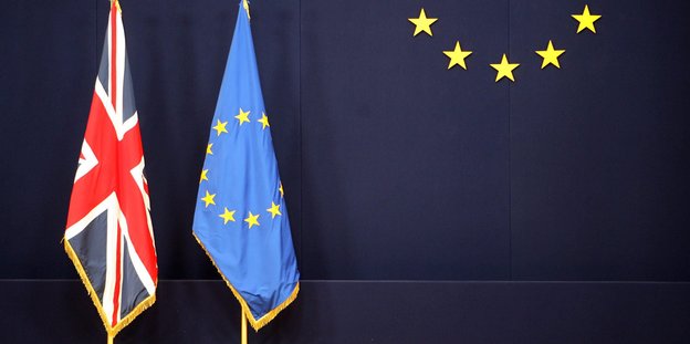 Die britische neben der europäischen Fahne, vor blaubem Hintergrund. Teil der europäischen Sterne an der Wand zu erkennen