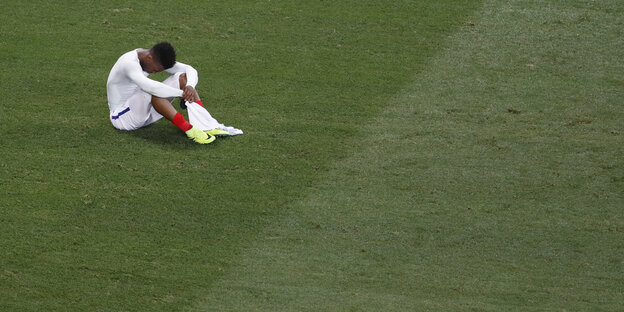 Ein Fußballer sitzt niedergeschlagen auf dem rasen