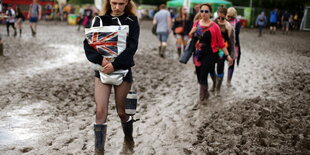 Besucherinnen laufen beim Glastonbury Festival durch den Matsch