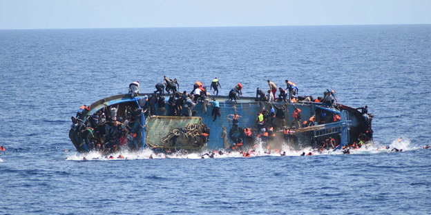 ein Boot mit vielen Menschen, das gerade im Meer versinkt. Viele Menschen sind schon ins Wasser gesprungen