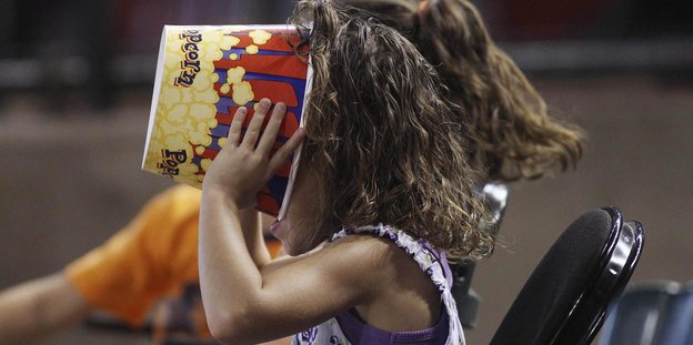 Mädchen steckt ihren Kopf in einen Popcornbehälter