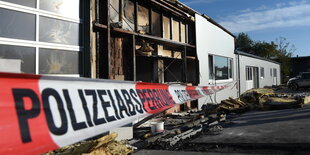 Polizei-Absperrband vor einer halb abgebrannten Halle