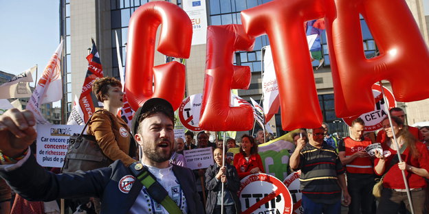 Menschen protestieren mit Schildern und roten Luftkissen, die die Buchstaben „CETA“ bilden