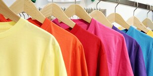 Mehrere bunte T-Shirts hängen auf Bügeln hintereinander auf einer Stange