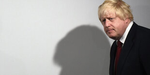 Ein Mann guckt nachdenklich. An der Wand ist sein Schatten abgebildet. Es ist Boris Johnson.