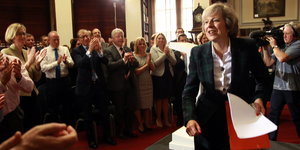 Theresa May in einem Raum mi Menschen, die ihr applaudieren