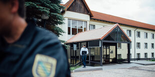 Ein Polizist steht vor einem langgestreckten Gebäude