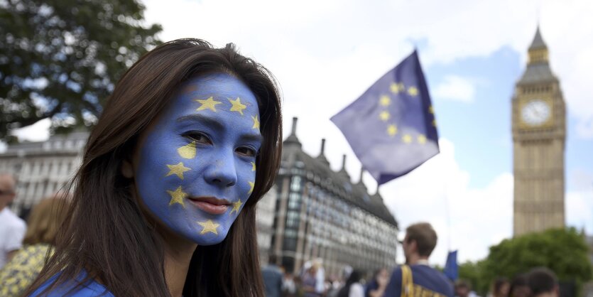 Eine Frau, deren Gesicht mit der Symbolik der EU-Fahne bemalt ist, dahinter der Big Ben