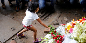 Ein Kind legt einen Strauß Blumen auf einen größeren Haufen mit Blumen
