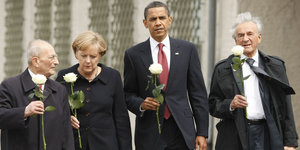 Angela Merkel, Barack Obama, Elie Wiesel und ein weiterer Holocaust-Überlebender in schwarzen Anzügen und mit je einer weißen Rose