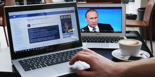 Zwei Laptops, auf dem Bildschirm des einen ist Putin zu sehen, auf dem anderen ist ein soziales Netzwerk geöffnet