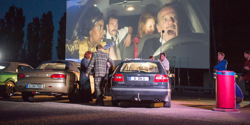 Menschen neben Autos vor einer Kinoleinwand