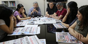 Männer und Frauen stehen auf einem Tisch, auf dem Zeitungen liegen