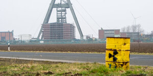 Förderturm eines Bergwerkes, im Vordergrund ein gelbes Fass mit Strahlenwarnzeichen