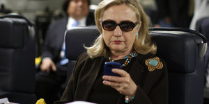 Hillary Clinton trägt eine Sonnenbrille und nutzt ihr Handy