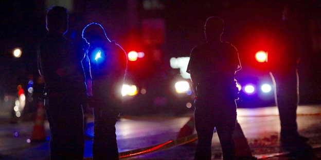 Blaulicht von US-Polizeiautos im Dunkeln, davor Silhouetten