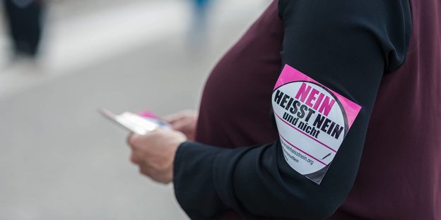 Eine Frau steht mit einer Armbinde mit der Aufschrift "Nein heißt Nein" vor dem Deutschen Bundestag