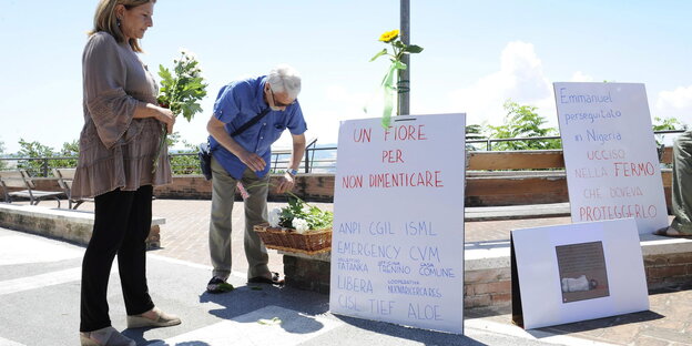 Zwei Menschen legen neben Schildern mit italienischer Aufschrift Blumen nieder