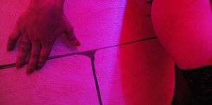 Hand und Körperteil vor einer Wand in düster-rosanem Licht
