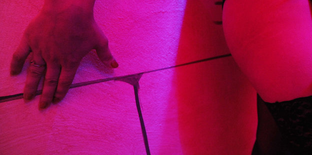 Hand und Körperteil vor einer Wand in düster-rosanem Licht