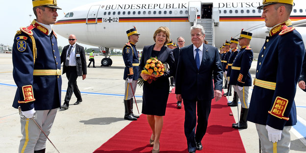 Bundespräsident Gauck und seine Lebensgefährtin laufen auf einem roten Teppich, dahinter ein Flugzeug, daneben Soldaten