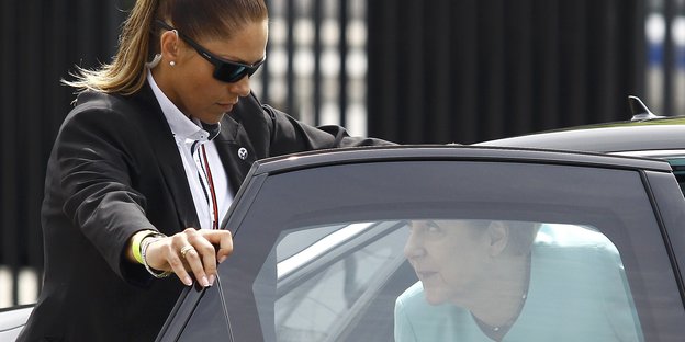 Angela Merkel steigt aus einem Auto, eine Bodyguard hält ihr dafür schützend die Tür auf