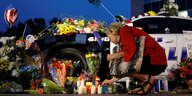 Eine Frau legt Blumen vor einem Polizeiauto nieder
