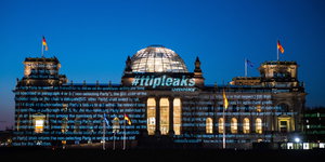 Der Bundestag wird von außen mit Text bestrahlt