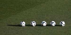 Fünf Fußballe liegen auf einem Rasenplatz
