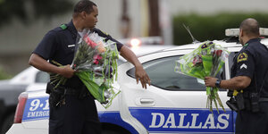 Zwei Polizisten vor einem Polizeiauto mit der Aufschrift "Dallas", beide haben je einen Blumenstrauß in der Hand