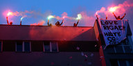 Menschen mit Kapuzen auf einem Dach, sie halten Pyrotechnik in den Händen