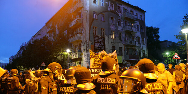 Viele Polizisten mit Westen und Helmen vor einem bemalten Haus am späten Abend