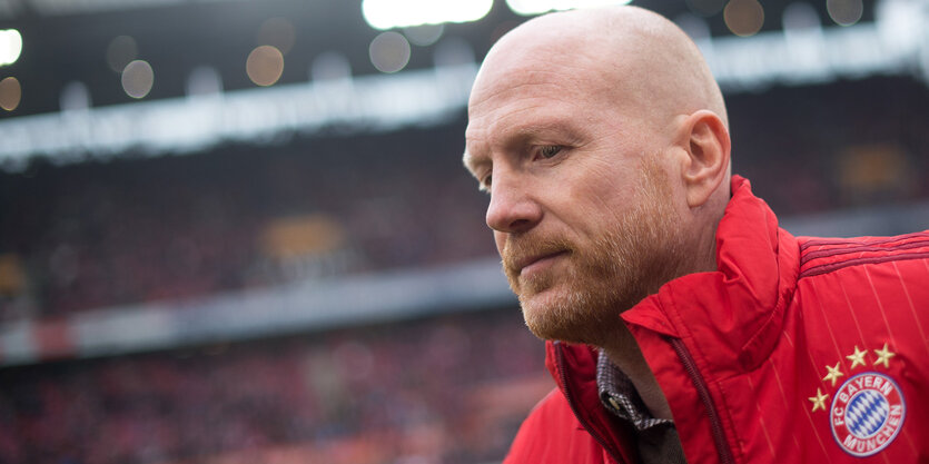 Ein Mann mit Glatze und roter Jacke in einem Fußballstadion