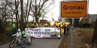Menschen demonstrieren mit Transparenten und Fahrrädern auf einer Straße, daneben das Straßenschild „Gronau“