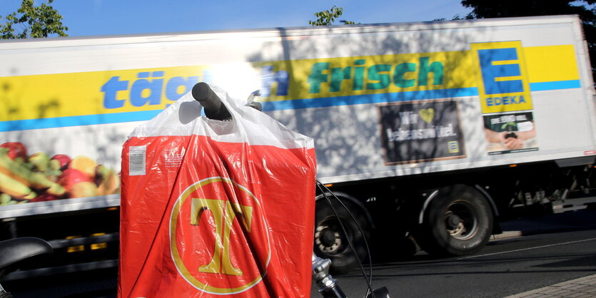 Ein Edeka-Lastwagen fährt an einem Fahrrad mit einer Tengelmann-Einkaufstüte vorbei