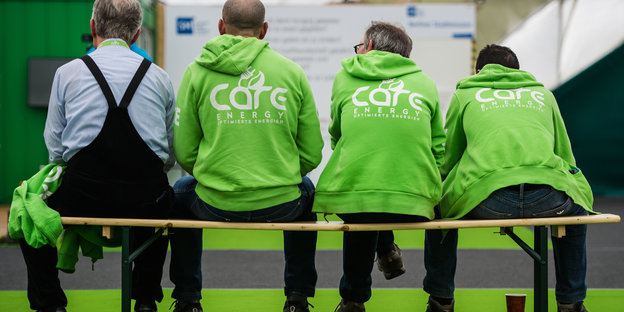 Mitarbeiter von Care-Energy sitzen in Jacken mit Unternehmensaufdruck auf einer Bank.