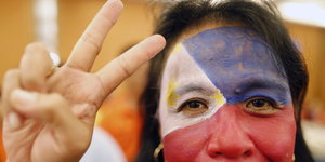 Eine Frau mit aufgemalter Phillippinen-Flagge im Gesicht, macht ein Peace-Zeichen mit der Hand