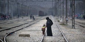 Eine Frau und ein Kind laufen über Bahngleise in Idomeni