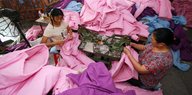 Frauen arbeiten an Nähmaschinen, umgeben von Textilbergen