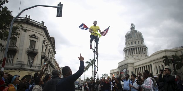 Ein Mann mit einer kubanischen und einer US-Fahne fährt auf einem Hochrad durch Havanna.