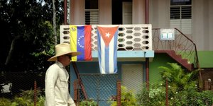 Ein Balkon mit einer kubanischen und einer venzolanischen Fahne. Im Vorderung ein Passant.